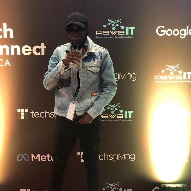 Godwill Barasa at the Techsgiving technology event in Nairobi, standing in front of a sponsor backdrop